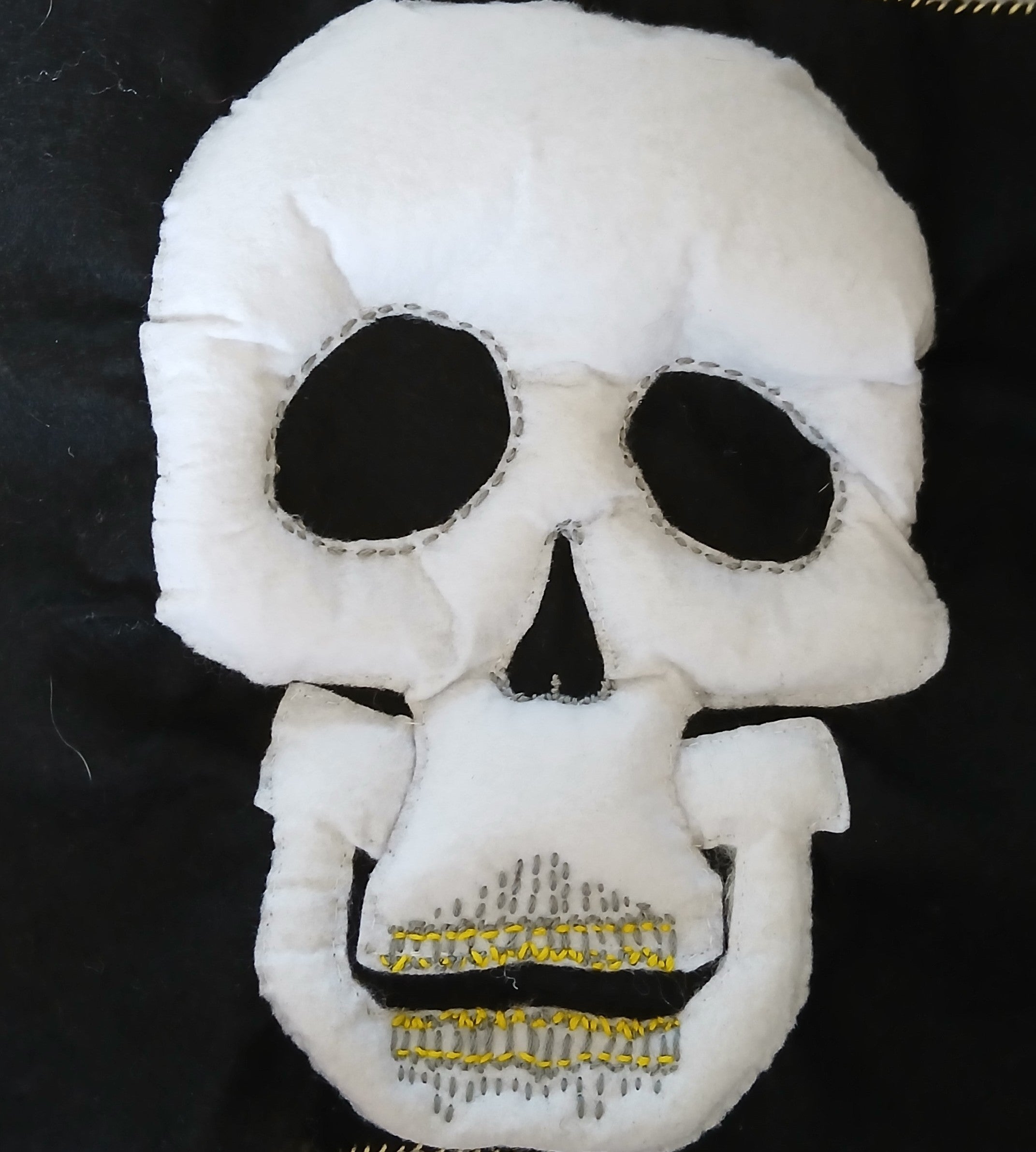 White skull-shaped plush toy with black details on a dark background