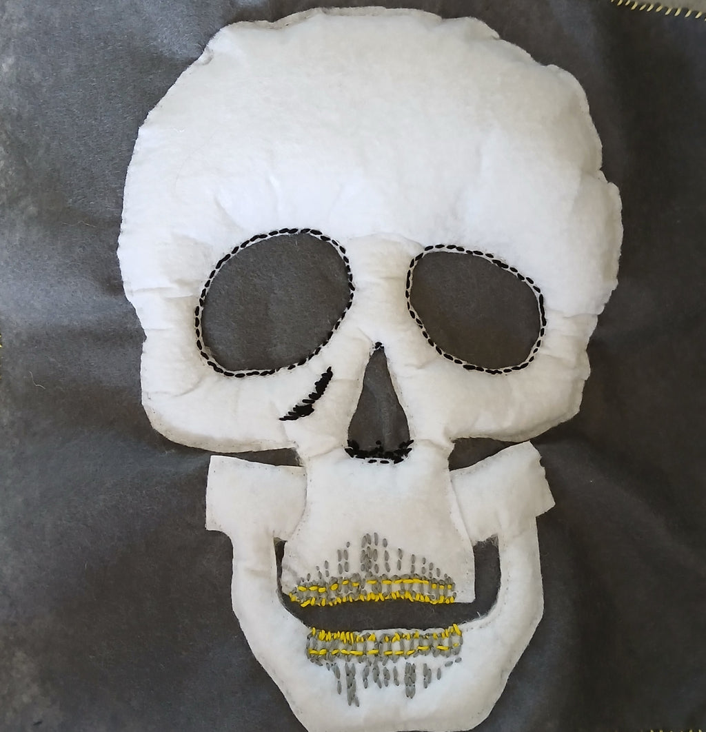 White skull-shaped pillow with black eye sockets and yellow teeth on a dark background