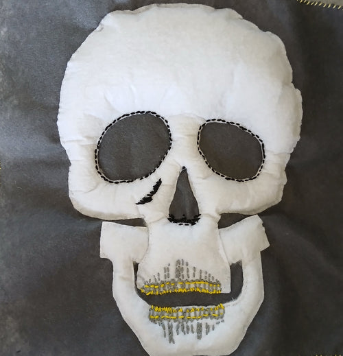 White skull-shaped pillow with black eye sockets and yellow teeth on a dark background